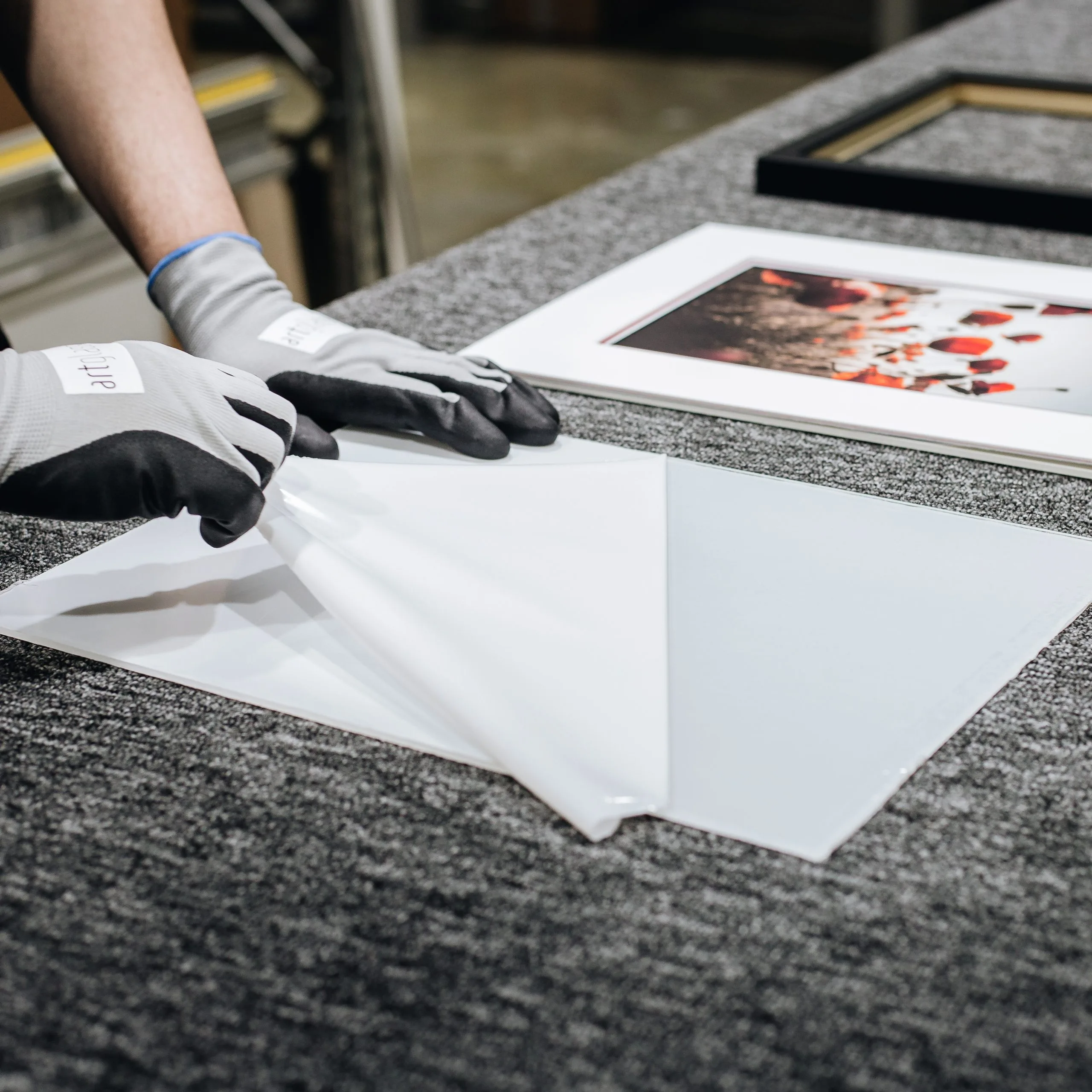 Framer in Artglass work gloves peeling protective film from a glass sheet in a framing workshop