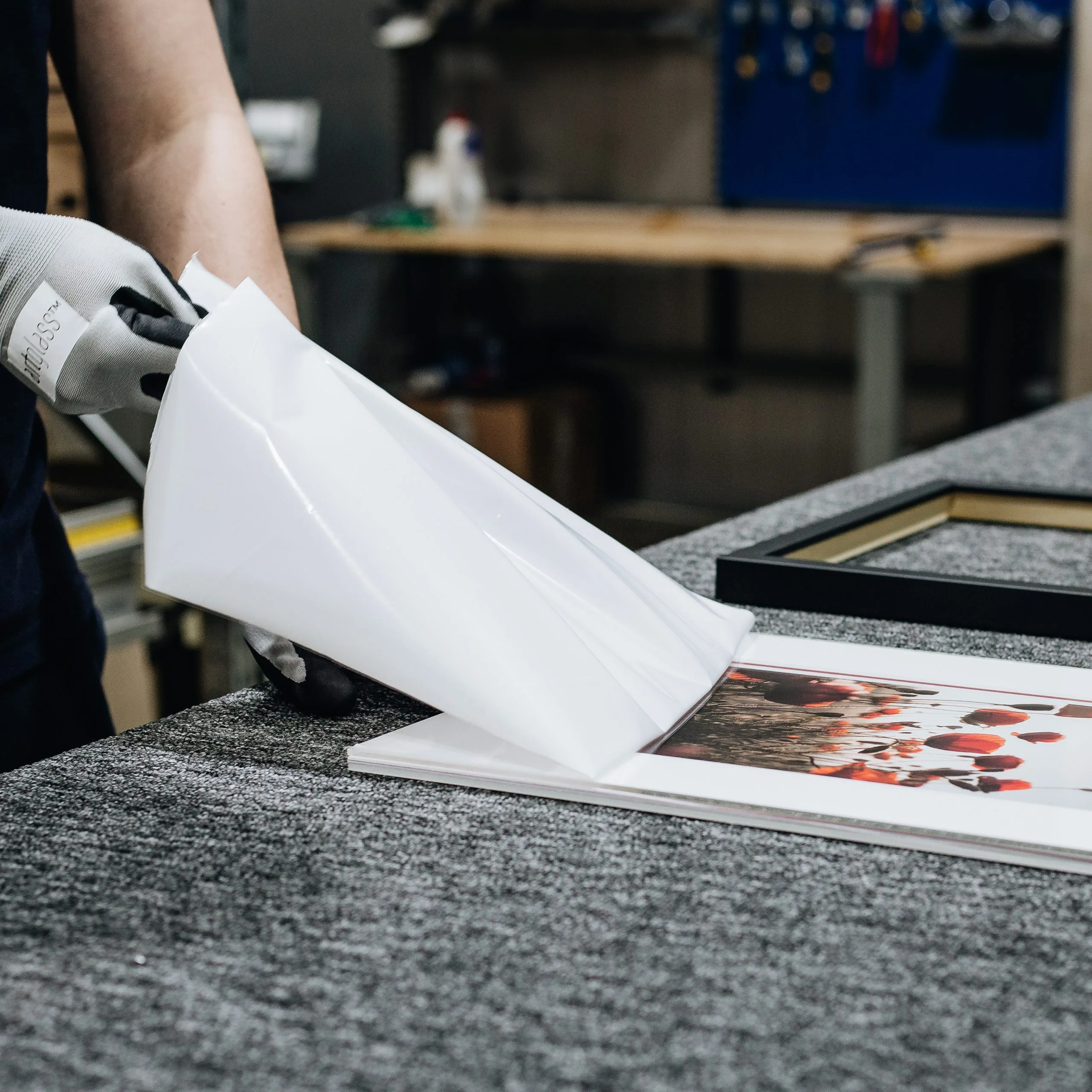 Framer peeling protective interleaving film from an Artglass sheet over a matted poppy print